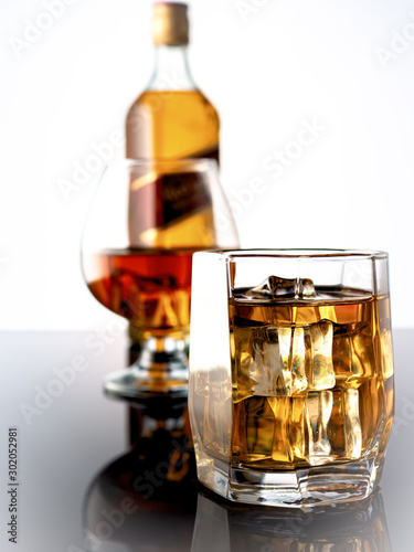 Glass of whiskey with ice on a dark background. In the background a glass with whiskey and a bottle of whiskey