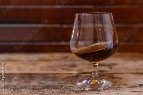 Glass of strong cognac drink on wooden background.