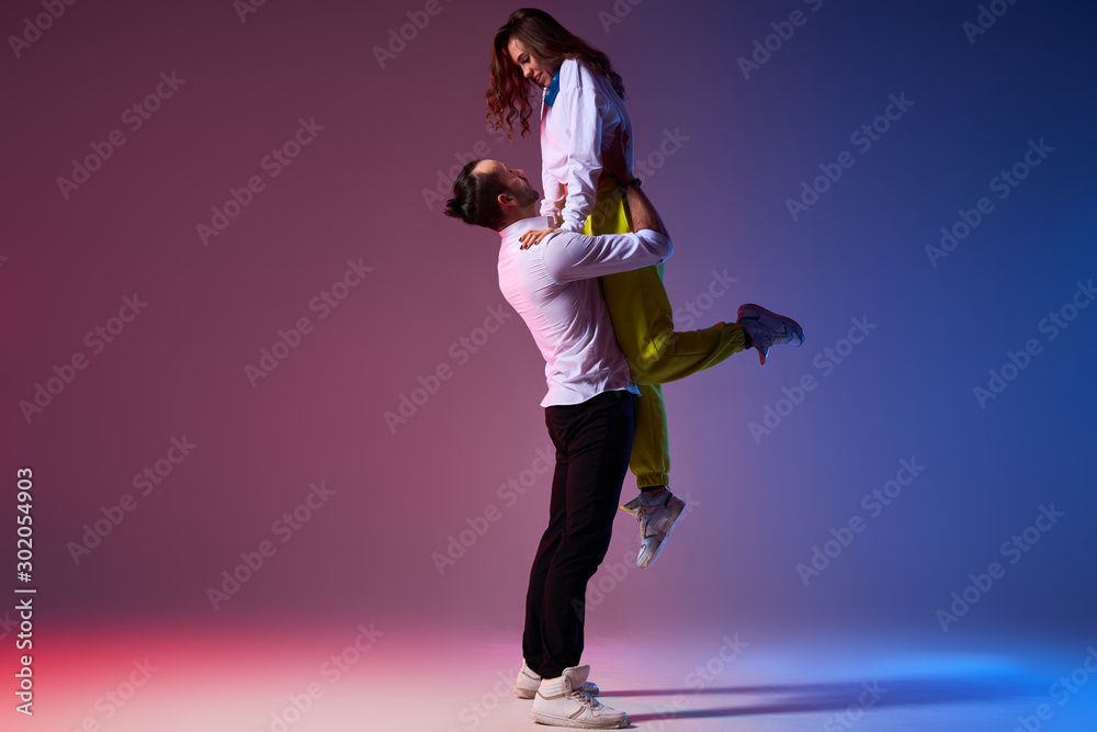 Strong active professional dancer holding slim attractive girl in hands, raising up, looking at female partner with passion, performing in dance show musical, flexible and weightless concept