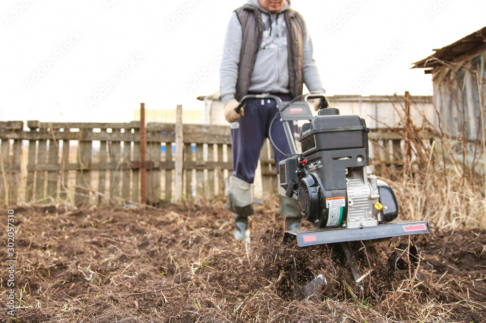 custom made wallpaper toronto digitalcultivating soil with gasoline cultivator. the farmer works the land before planting. man digs the ground with a diesel cultivator. farmer cultivates the land by a moto cultivator