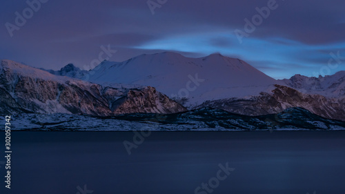Snowy mountains by a fjord in northern Norway in winter at bluish low evening light
