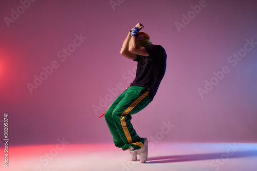 Fotografie Modern hip hop dancer frozen in movie, standing on tiptoe, covering head with ha