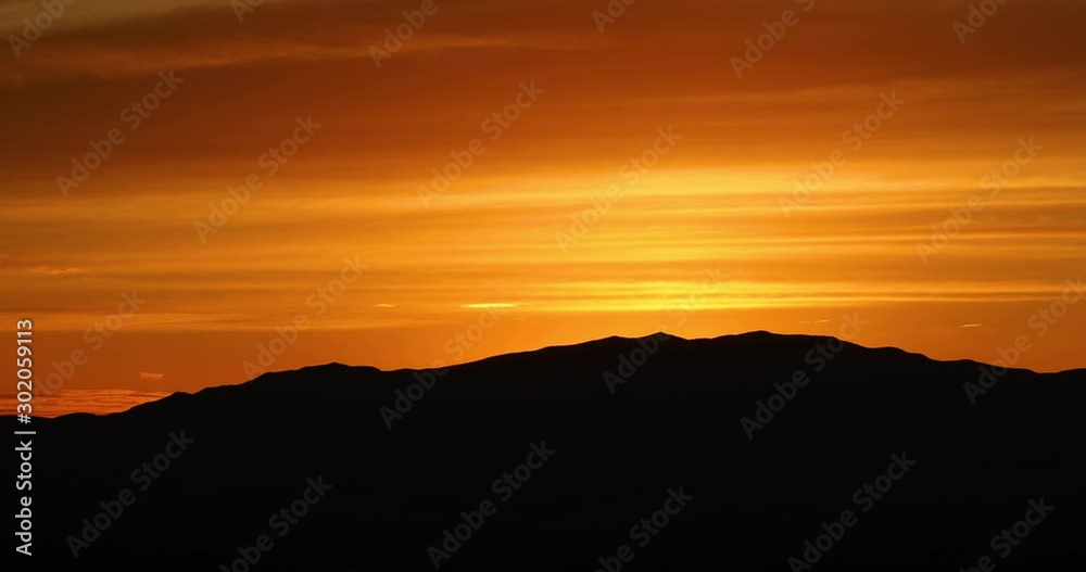 Brilliant orange sunset over desert mountain. Late evening orange golden sun sets over desert mountain peaks in southern Utah near St George. Outdoor nature, environment and beauty. Brilliant orange sunset over desert mountain. Late evening orange golden sun sets over desert mountain peaks in southern Utah near St George. Outdoor nature, environment and beauty.