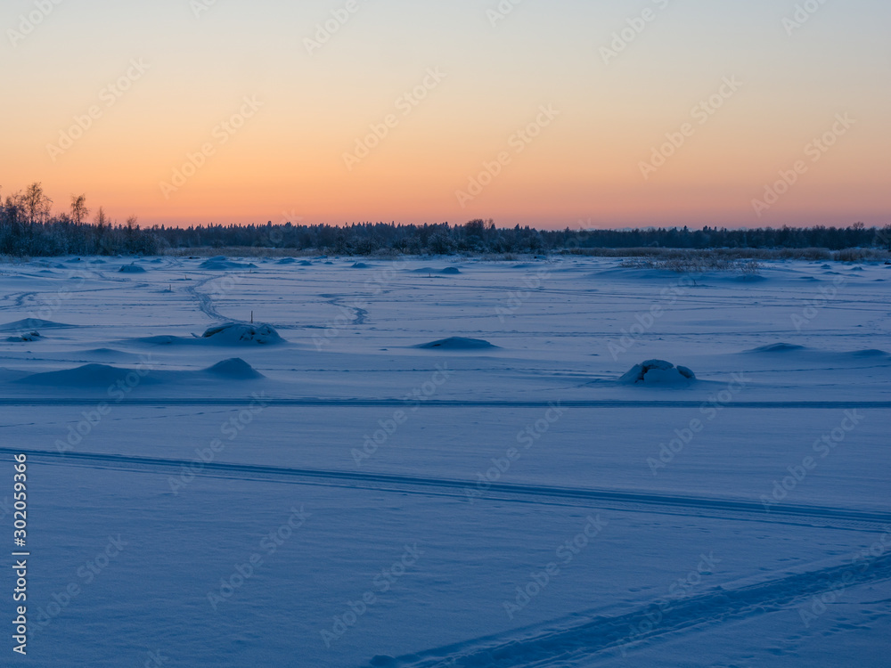 Snowy frozen sea with ski tracks in Finland at sunset time
