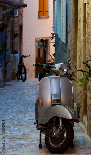 An old silver moped parled on a narrow pawed street in Italy.