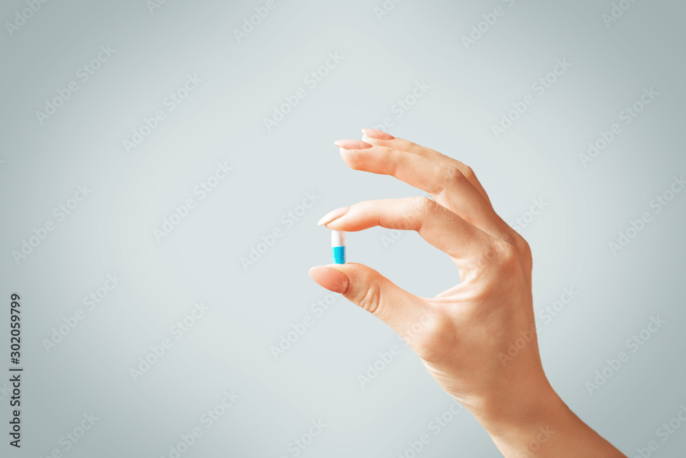 Female hand holding a capsule pill or vitamin. - obrazy, fototapety, plakaty 