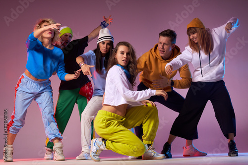 Beautiful female leader of dancing teen with long wavy hair dressed in bright yellow pants and white long sleeve clothes sitting in the middle with knee on floor, looking straight with calm face, photo