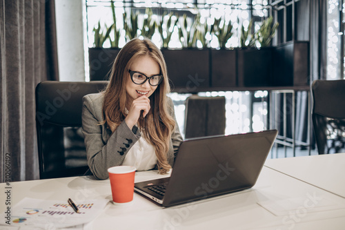 Cute young businesswoman is contented with the results she sees on a laptop screen