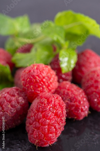 Vertical close-up of wet raspberries with mint leaves out of focus on black slate