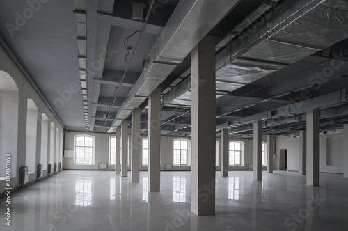 Huge empty open space in the old factory building with rows of columns, large windows and pipes under the ceiling. Industrial or loft style background, mock up