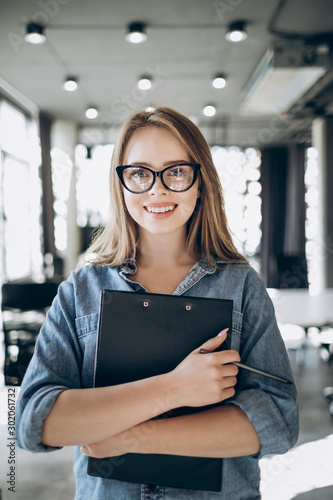 Portrait of young cute female office employee standing with a clipboard in her hands
