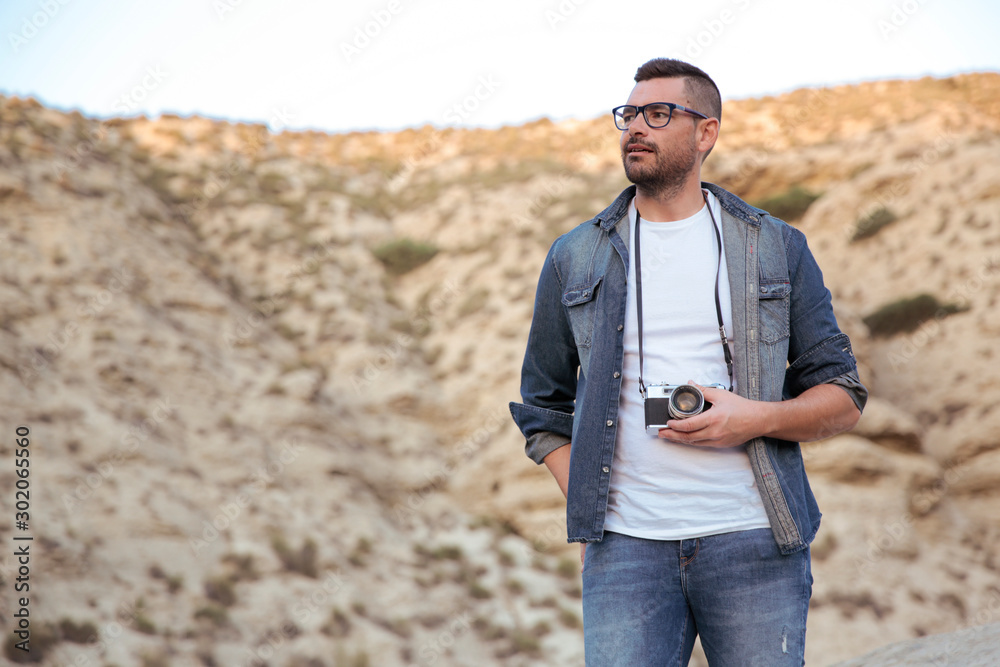 Hombre joven con lentes y ropa vaquera sujetando cámara de fotos analógica  al aire libre Stock Photo | Adobe Stock