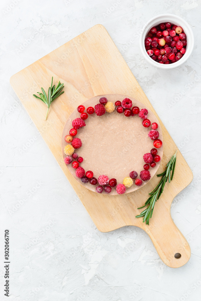 Raw cake decorated with raspberries and rosemary on a wooden board. Gluten free, vegetarian food.