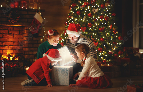 Merry Christmas! happy family mother father and children with magic gift near tree at home.