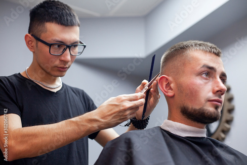 guy get a haircut in a barbershop, a young Kazakh barber cuts manually with scissors and a comb, the master makes a short haircut at the hairdresser