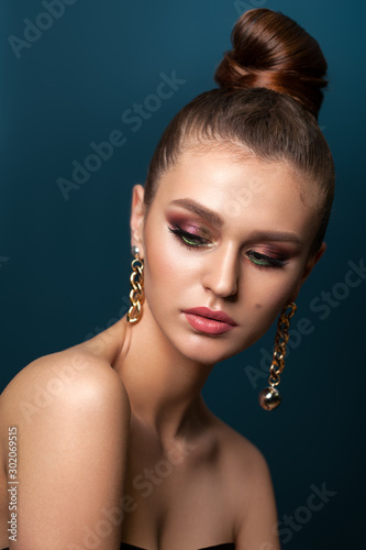 Beautiful elegant young girl with bright colorful trendy smoky eyes, bun hairstyle and trendy gold earrings