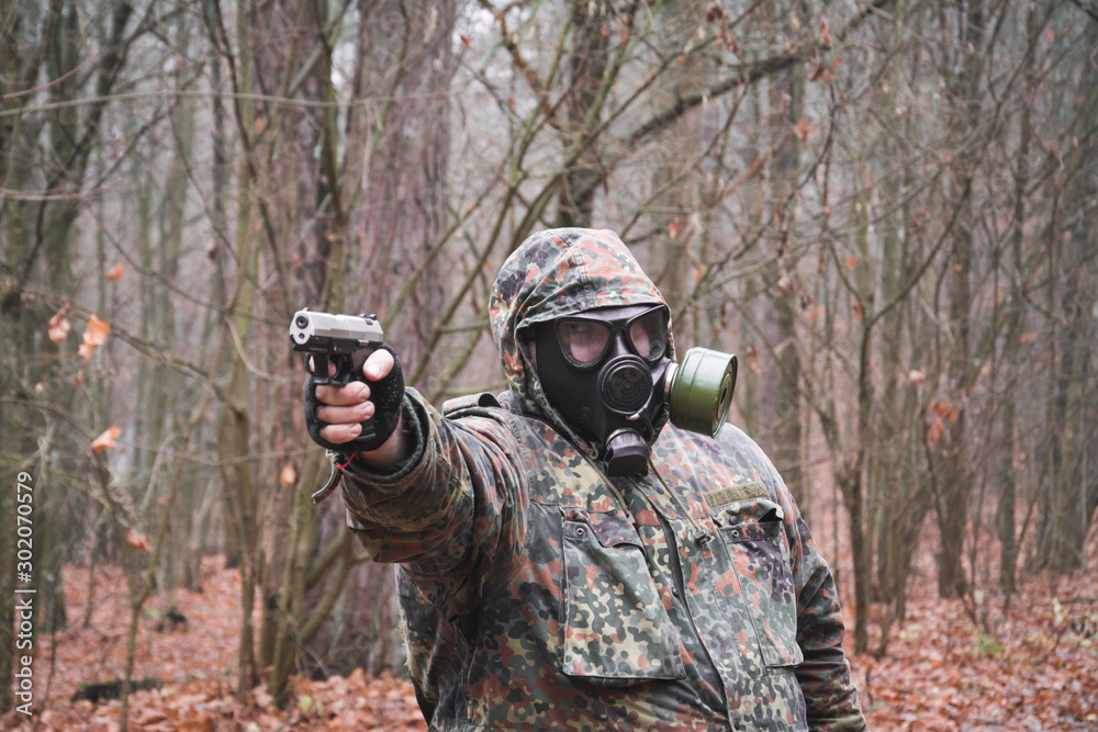 Fototapeta premium A military man in a gas mask and with a gun aims at the target