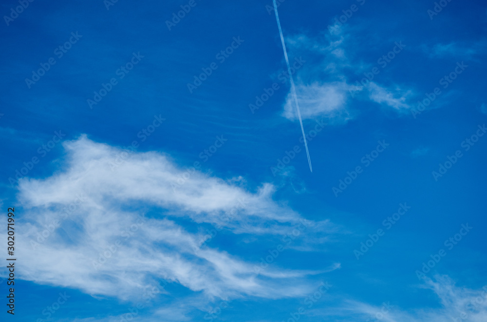 Blue sky with clouds and trail from a flying airplane. In the sky a trace from a flying airplane. Blue sky with clouds and trail from a flying airplane. In the sky a trace from a flying airplane.