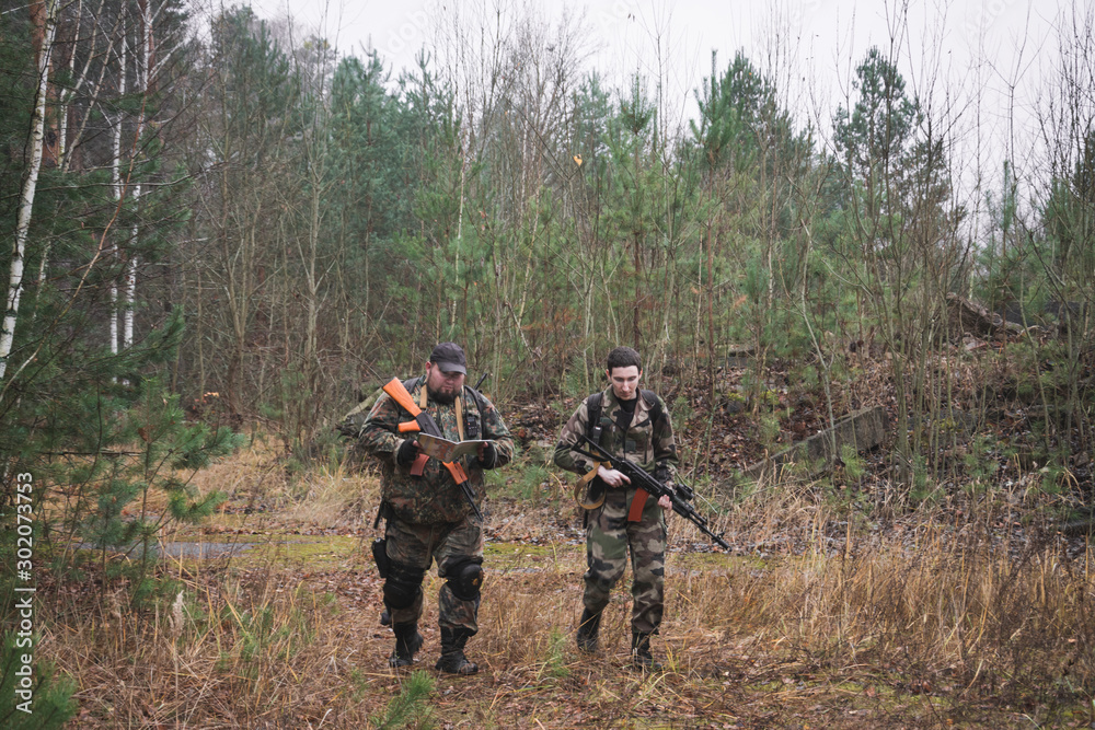 two armed soldiers in the autumn forest move along a forest road with weapons in their hands