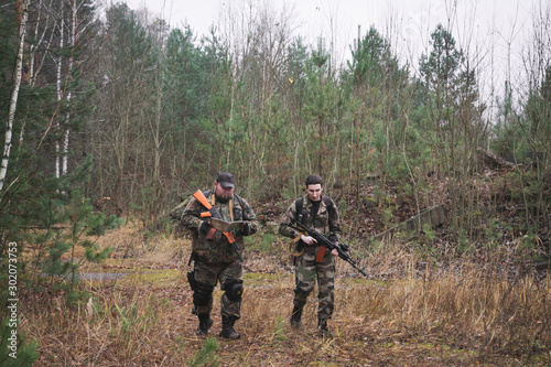 two armed soldiers in the autumn forest move along a forest road with weapons in their hands