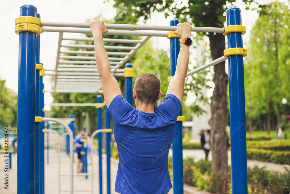 Obraz premium Man doing pull ups workout in the ground park. View from back.