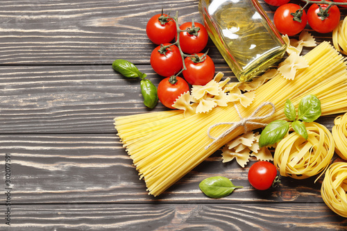 Composition with different Uncooked pasta, ingredients for sauce. cherry tomatoes, spices, oil, basil on a wooden background. top view. Place for text.