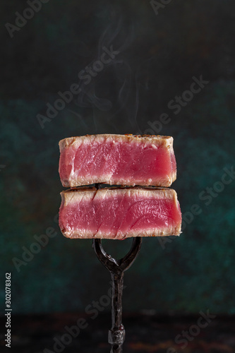 Slices of rare roasted tuna steak on vintage fork on dark background with copy space