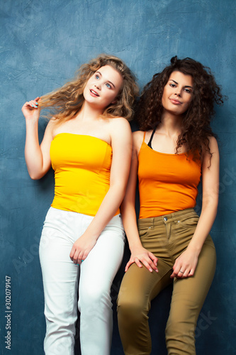 young pretty teenage girls friends with blond and brunette curly hairs posing cheerful on blue background, lifestyle people concept © iordani