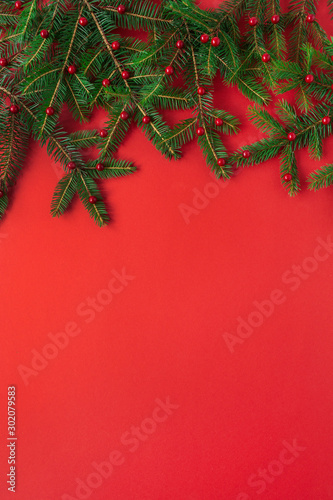Christmas   New Year composition. Fir-tree branches with red berries on red background. Flat lay  top view creative festive concept.