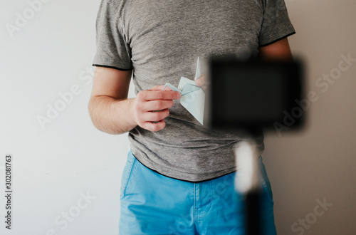 The man is recording a video with instructions on how to fold origami. Influencer concept, recording movies on social networks. Camera directed at blogger.