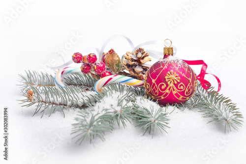 Red Christmas bauble with gold ornament, decorative berry and gilded pine cone on white background with natural fir twigs under snow. Merry Xmas and a Happy New Year!