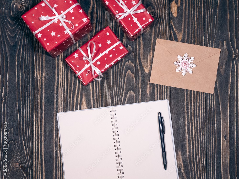 Christmas gifts wrapped in red paper with white stars, notebook and letter on wooden background. Holiday preparation, top view Christmas gifts wrapped in red paper with white stars, notebook and letter on wooden background. Holiday preparation, top view