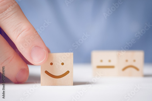 A man holds a wooden cube with a positive face on a neutral and negative background. Concept for evaluating an action or resource. photo