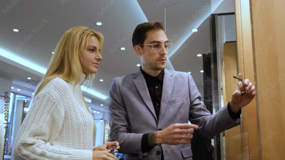 Attractive blond woman is asking for store consultant to try pair of glasses from showcase. She is trying on them. Attractive blond woman is asking for store consultant to try pair of glasses from showcase. She is trying on them.