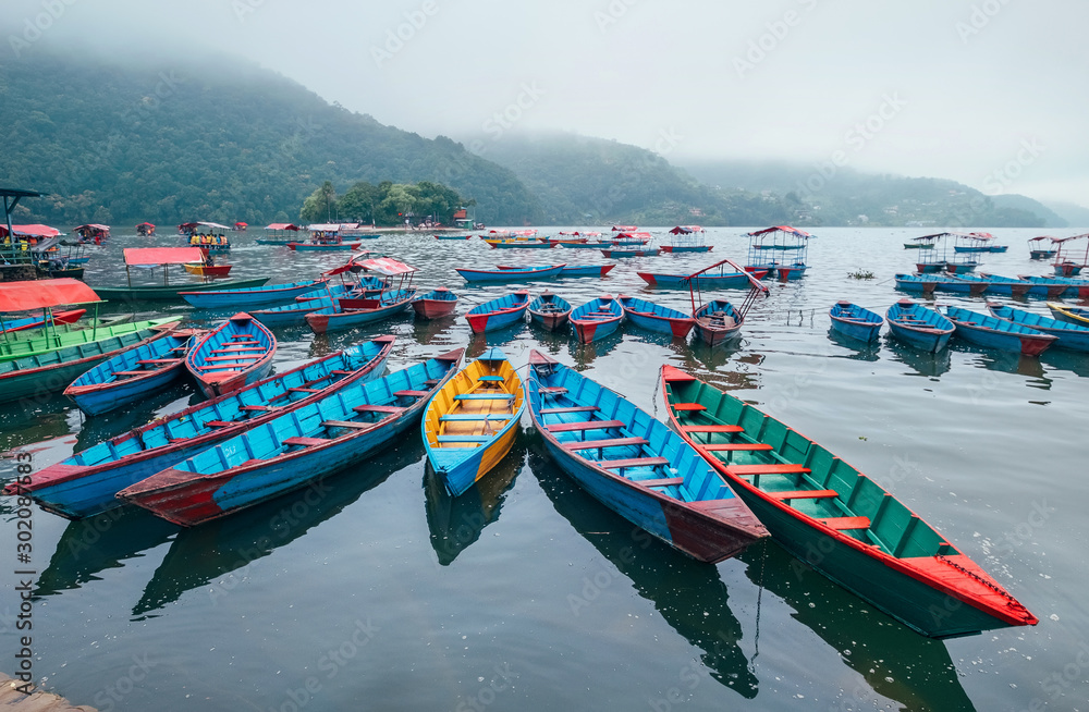 Multicolored traditional rowboats on the morning lake water in Pokhara, Gandaki Pradesh, Nepal. Asian traveling concept image.