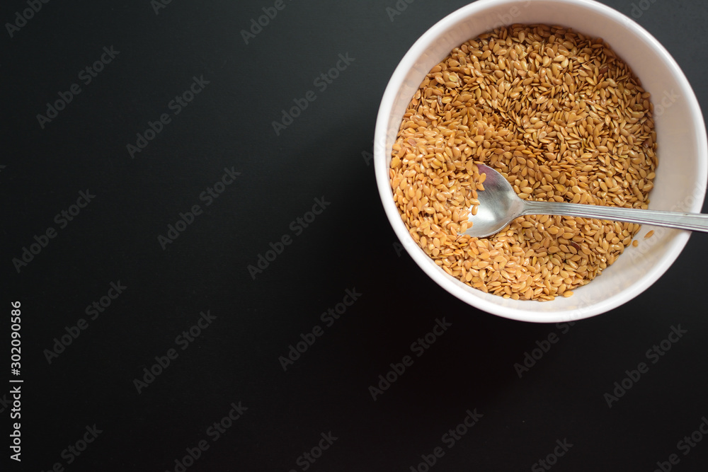 Bowl of flaxseeds with spoon over black background from above Bowl of flaxseeds with spoon over black background from above
