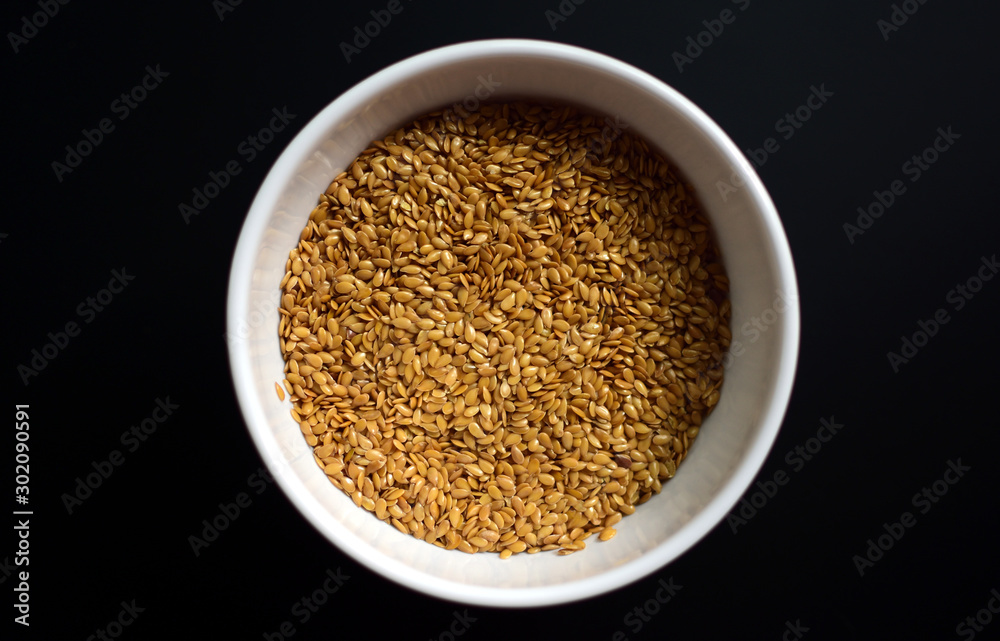 Bowl of flaxseeds with spoon over black background from above Bowl of flaxseeds with spoon over black background from above