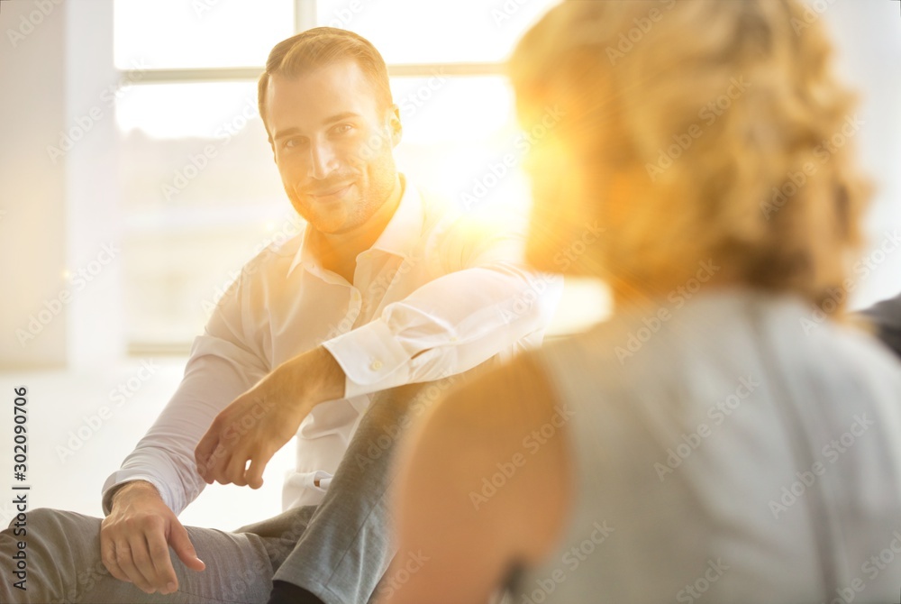 Obraz premium Handsome young businessman smiling while sitting on the floor with collegues in new office