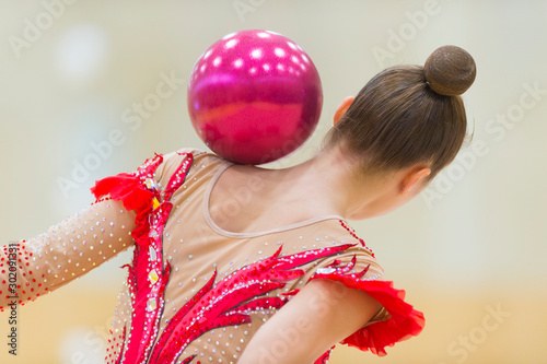 girl with a ball on a professional gymnast .Flexibility in acrobatics and fitness health. Workout of girl on gold background.