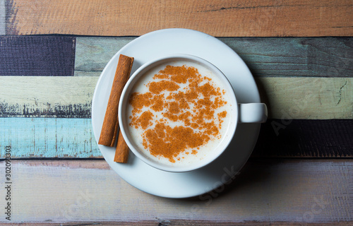 Top view white cup of salep milky hot drink of Turkey with cinnamon sticks and powder on wooden backdrop photo