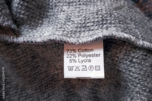 Wrong side of a gray dress made of wool, the composition is specified: cotton, polyester and lycra. Fabric composition clothes label on gray texture background.