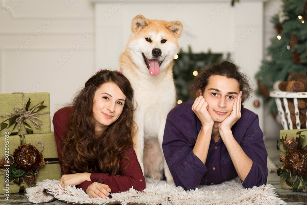 Young happy couple cuddling adorable akita inu dog with on the floor for Christmas holidays at home.