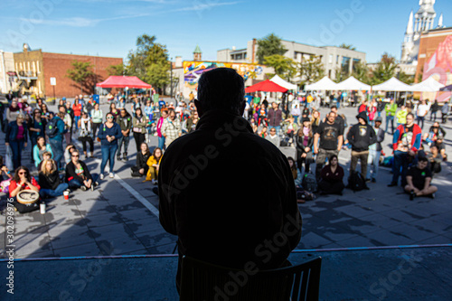 Silhouette of man talking to crowd at open public space. People standing and sitting listening to lider at background. Climate change protest photo