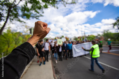 First person perspective and Selective focus on man fist raised during an ecological protest. Crowd of people walking with security in the background photo