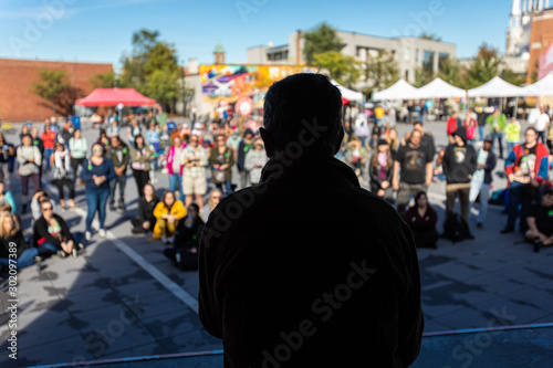 Silhouette of man on a stage talking to a crowd in a public space. People standing and sitting listening to his discourse during climate change protest photo