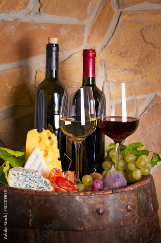 Wine with cheese, prosciutto and fruits beside old barrel in wine cellar. Wine tasting concept