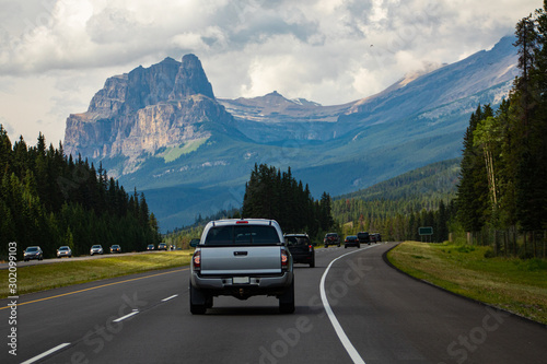 cars, pickups and SUVs are traveling accross the canadian rockies on a 4 lane highway. High mountain peaks and dense clouds in the background