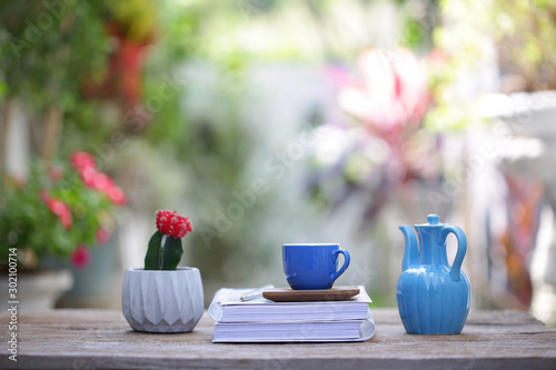 Blue cup with small cactus plant and diary notebook with blue jar on wooden table at outdoor