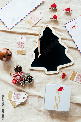 Christmas blackboard with a form of a christmas tree on a juta background, christmas ornament atop of it, orange candieds, mistletoe ,cinnamon  sticks and a box with ho ho ho text greetings,top view+ photo