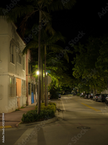A dark and quiet street illuminated by street lights at night. Miami, Florida, USA © christian